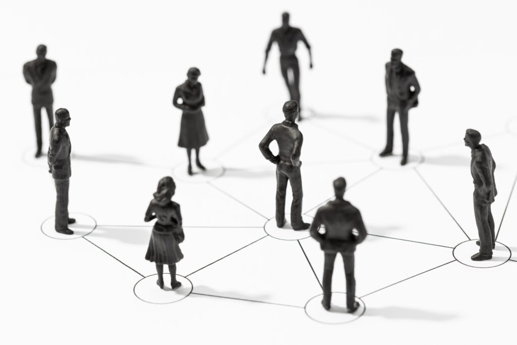 A group of tiny figurines stand on a white surface with black lines connecting them representing professional networks.